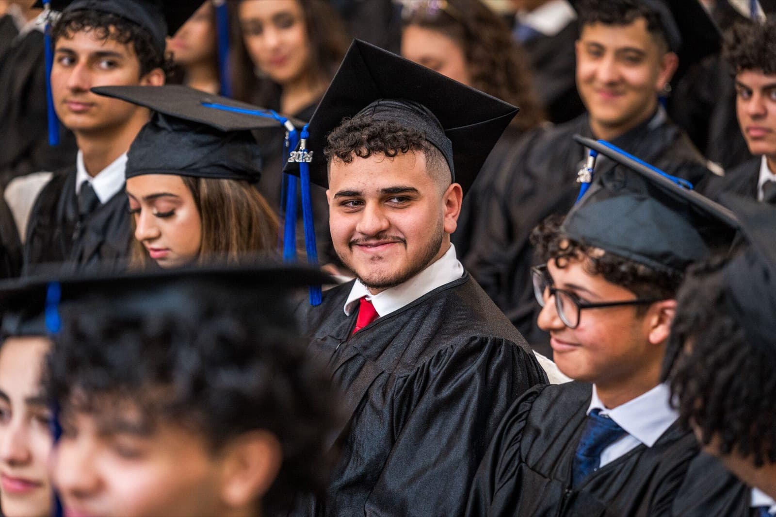 Smiling graduates in gowns and mortarboards sit together during the ceremony.