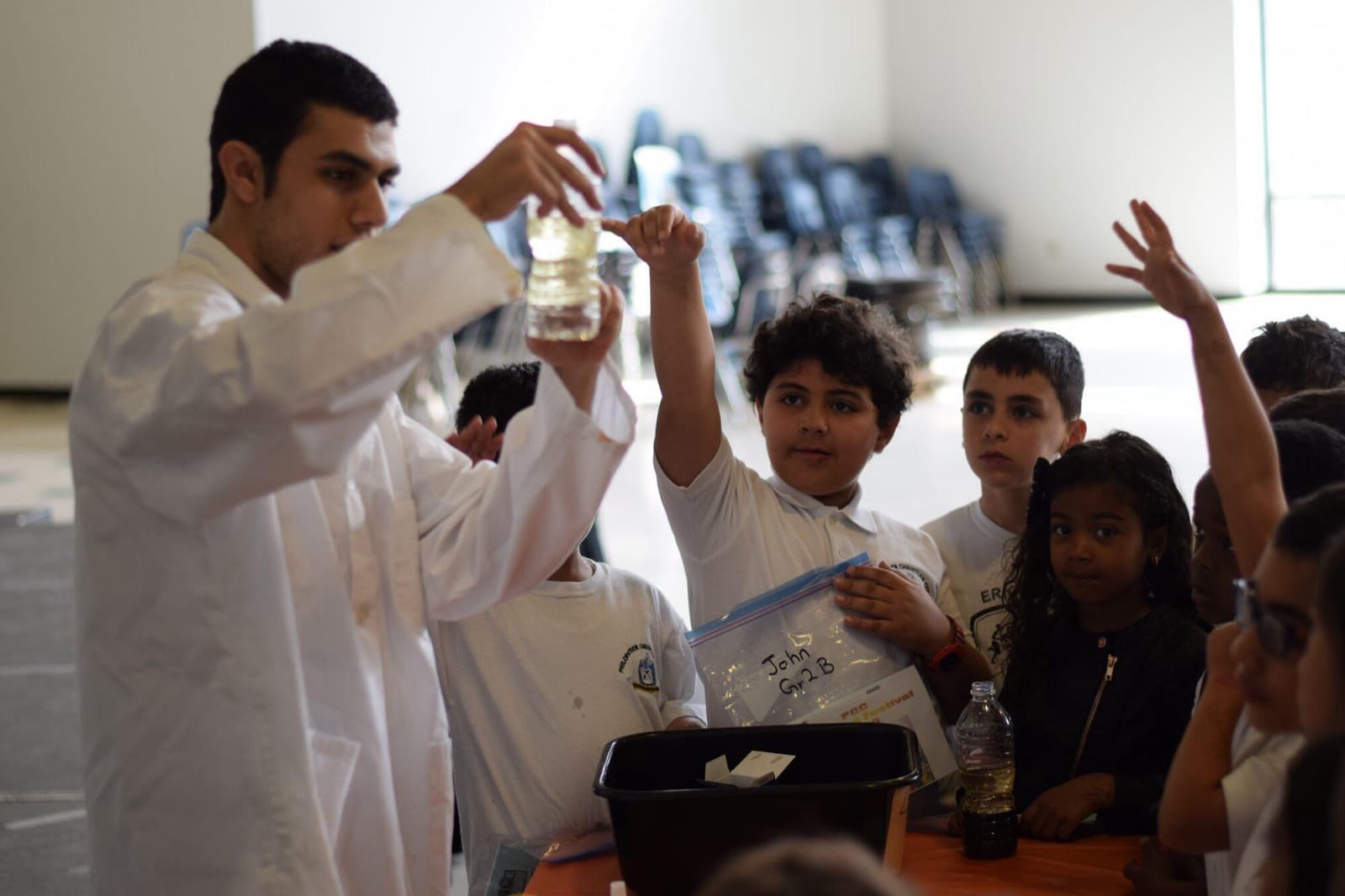 A teacher in a lab coat shows a sample to a group of younger students.