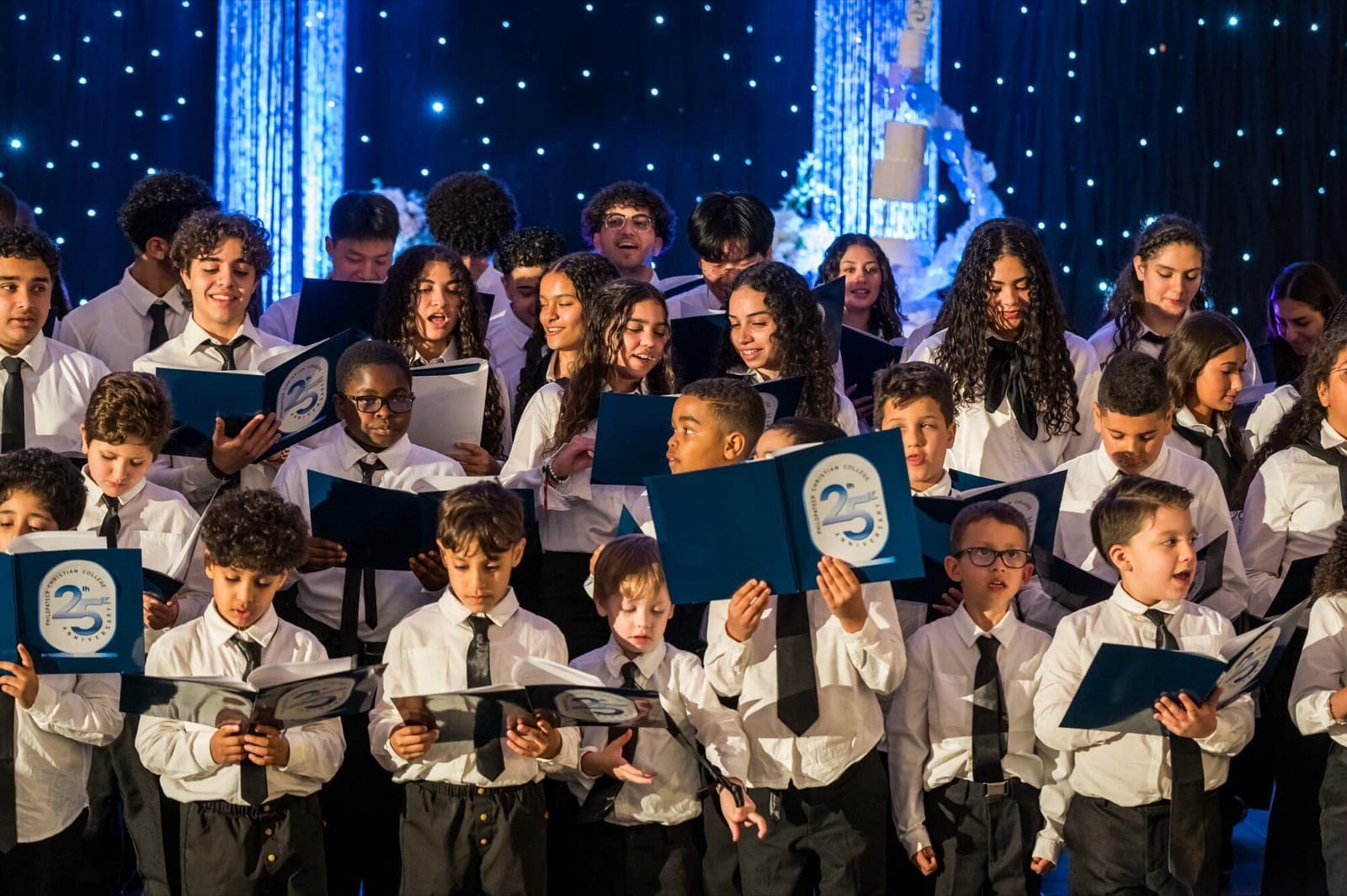 A student choir sings from blue folders on a starlit stage at the anniversary gala.