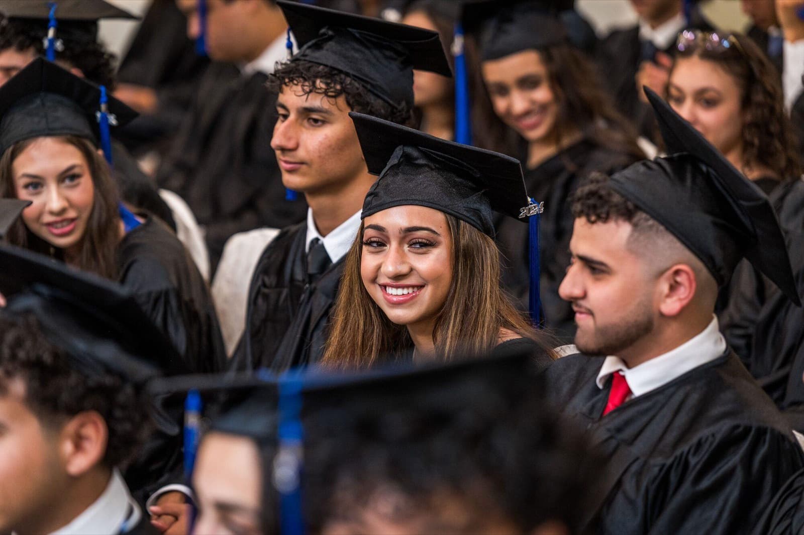 Graduates in caps and gowns sit close together, a young woman smiling at the camera.